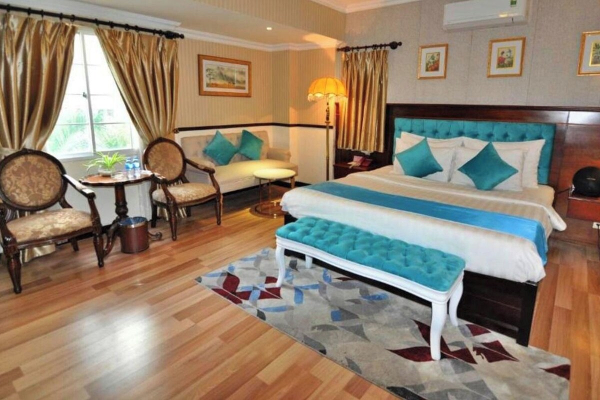 A hotel room with a large bed, a sitting area with a table and chairs, and a view of the outdoors.