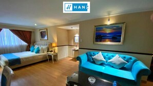 A hotel room with a bed, a blue sofa, a small table, and a painting on the wall. - S79 Vuon Saigon Hotel & Spa (Ho Chi Minh City)