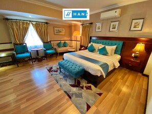 A hotel room with a large bed, a sitting area with a sofa and chairs, a small table, and a nightstand with a lamp. - S79 Vuon Saigon Hotel & Spa (Ho Chi Minh City)