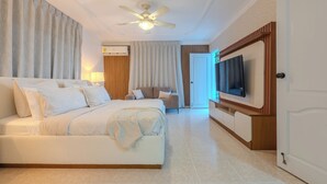 A hotel room with a bed, a TV, a ceiling fan, and a door. - Elegant 4BR Home w/ Private Pool (Santiago De los caballeros)
