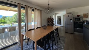 A modern kitchen with a built-in microwave and refrigerator, a dining area with a wooden table and chairs, and a large sliding glass door leading to an outdoor deck. - Villa Olivia 10 minutes from Palombaggia without traffic jams (Porto-Vecchio)