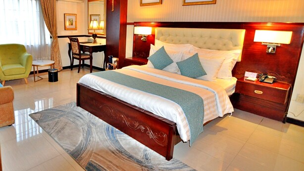 A hotel room with a large bed, a desk, a chair, and a small table.