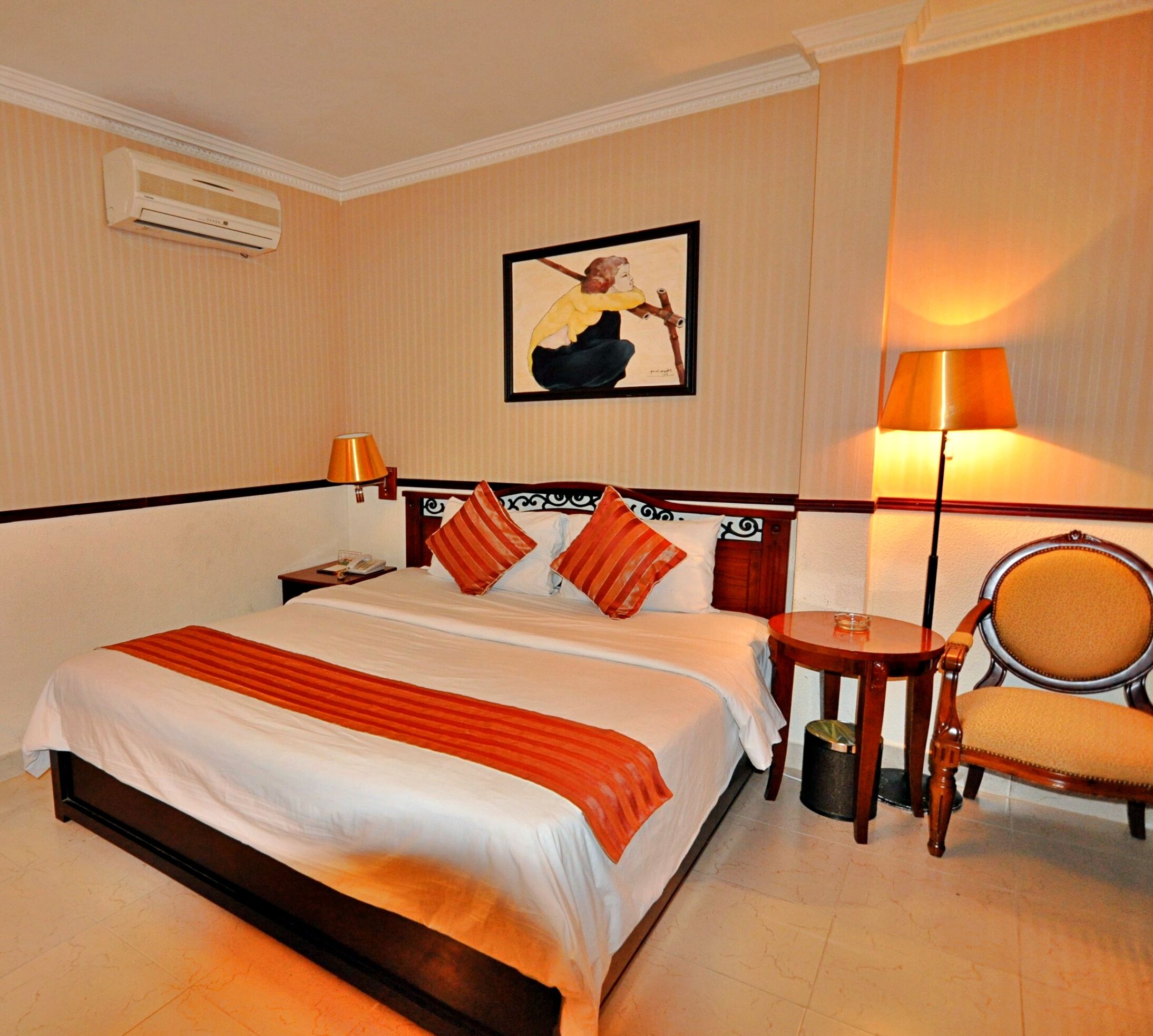 Habitación de hotel con cama, mesita de noche, lámpara, silla y un cuadro en la pared.