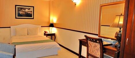 A hotel room with a bed, a desk, a chair, a lamp, and a mirror.