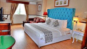 A hotel room with a large bed, a desk with a computer, a chair, and a small table.