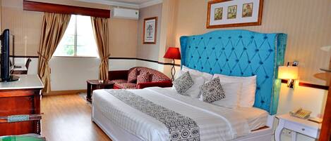 A hotel room with a large bed, a desk with a computer, a chair, and a small table.