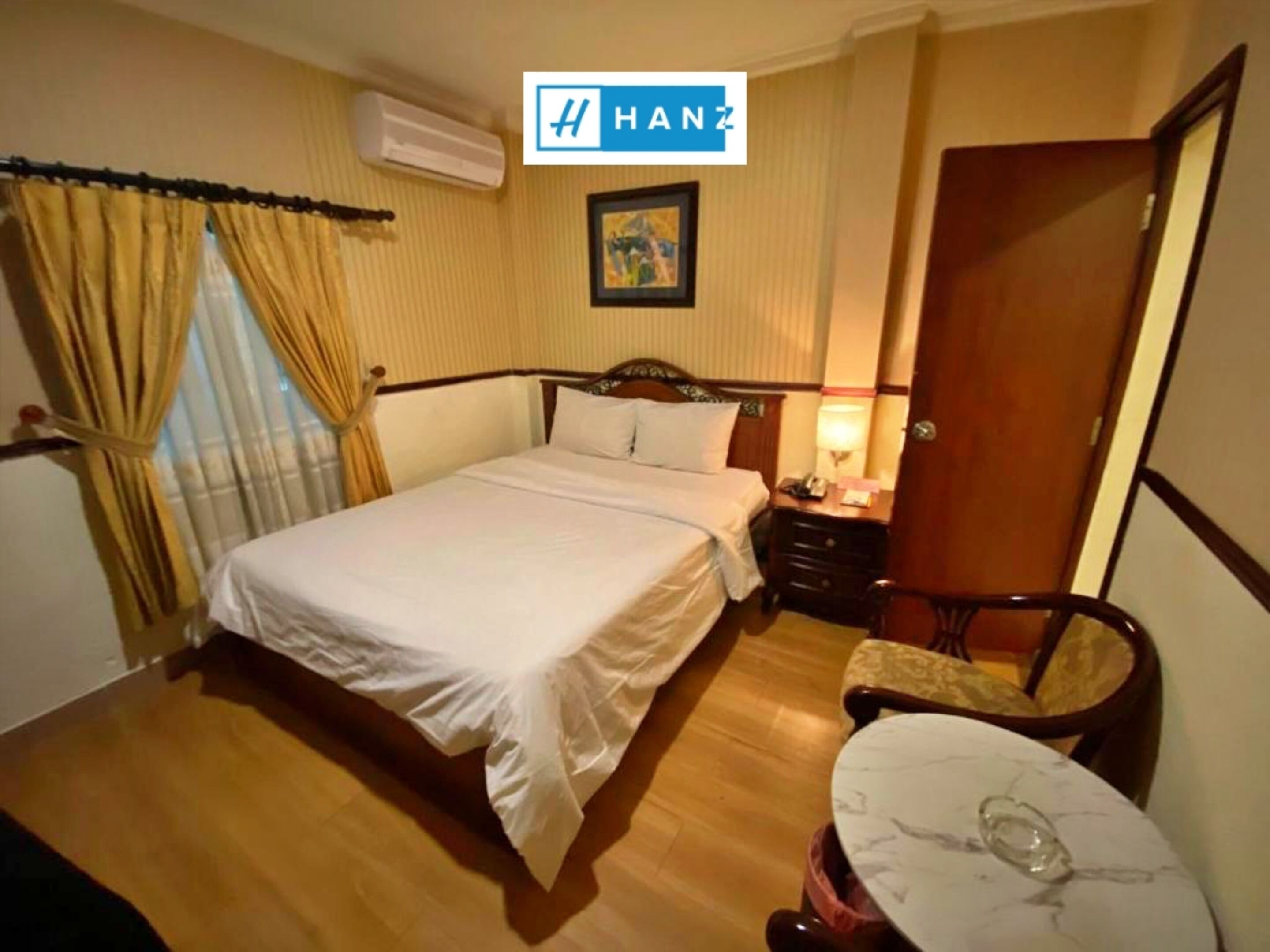 Camera d'albergo con un letto, un comodino, una lampada e un tavolino rotondo con un bicchiere sopra.