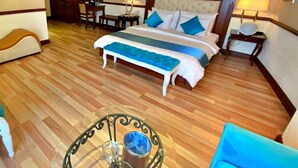 A hotel room with a large bed, a desk, a chair, a small table, and a painting on the wall.