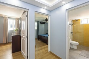 Une chambre d’h ôtel avec un plancher en bois, un lit, une salle de bain avec douche et une fenêtre avec des rideaux.