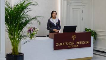 A reception desk with a nameplate reading "ZARAFSHON PARKSIDE RECEPTION," a laptop, and a potted plant.