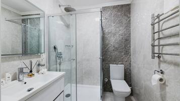 Une salle de bain moderne avec une douche à parois de verre, un lavabo blanc et un mur recouvert de carreaux de marbre.