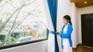 A room with a large window, a blue curtain, and a person adjusting the curtain. - Hoi An Nguyen Homestay (Da Nang)