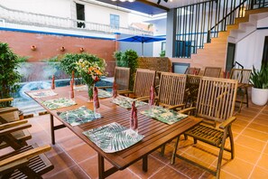 A patio area with wooden tables and chairs, a small fountain, and potted plants.