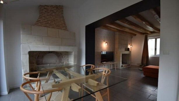 Un intérieur moderne avec une cheminée en pierre, une table à manger en verre, des chaises en bois et un coin salon confortable avec un canapé et un téléviseur.