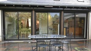 Un espace patio avec une table ronde et quatre chaises, de grandes portes-fenêtres coulissantes et un sol carrelé.