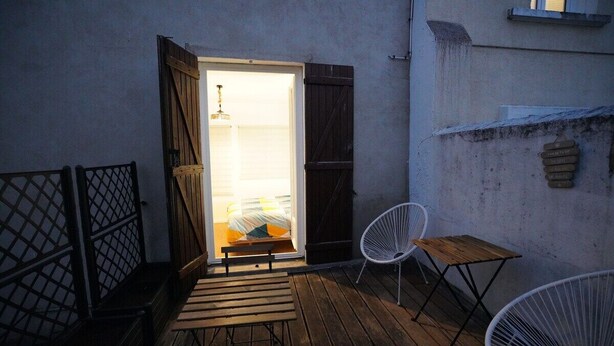 Un patio al aire libre con un banco de madera, una silla blanca y una mesita.