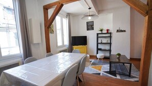 Comedor con una mesa cubierta con plástico, sillas grises, una mesa negra y una estructura de techo de madera.