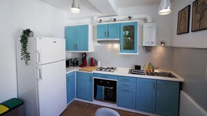 Una cocina compacta con armarios azules, un refrigerador blanco, una estufa a gas y un horno empotrado.