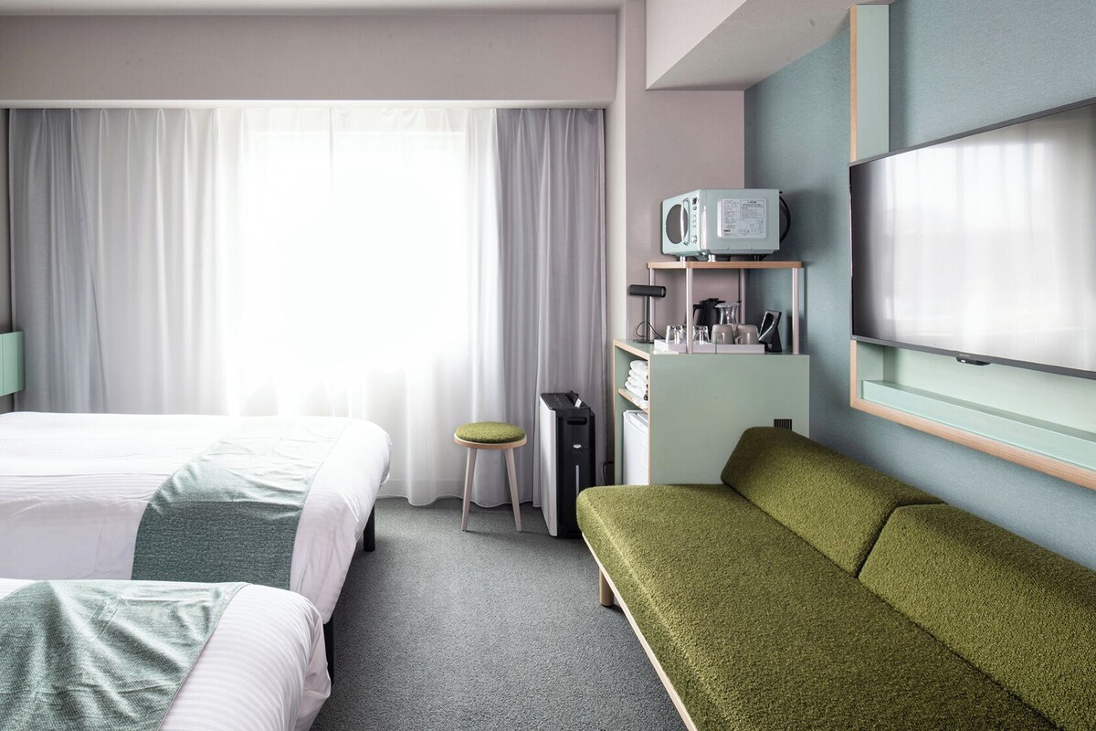 A hotel room with two beds, a desk, a chair, a TV, and a window with curtains.