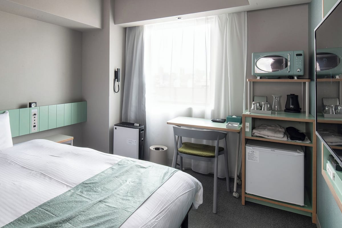 Habitación de hotel con cama, escritorio, silla, minibar y ventana con cortinas.