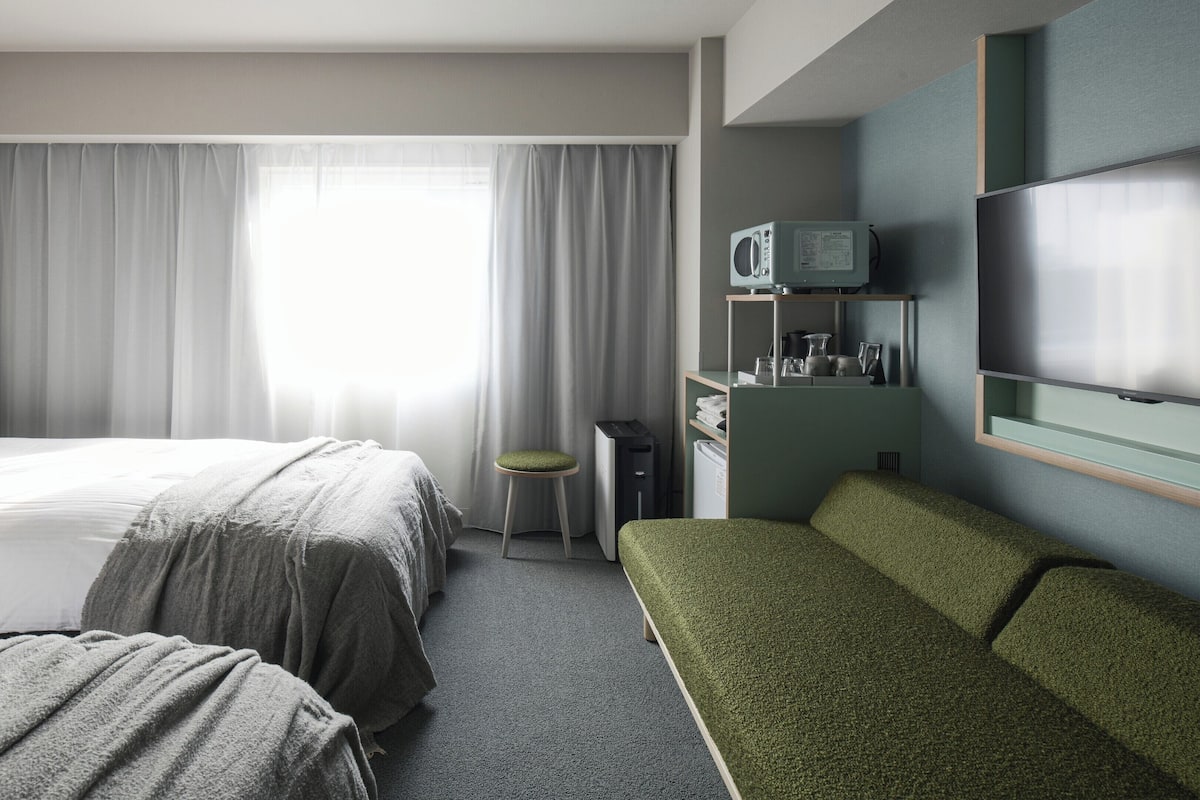 Habitación de hotel con dos camas, un escritorio, televisor y zona de estar.