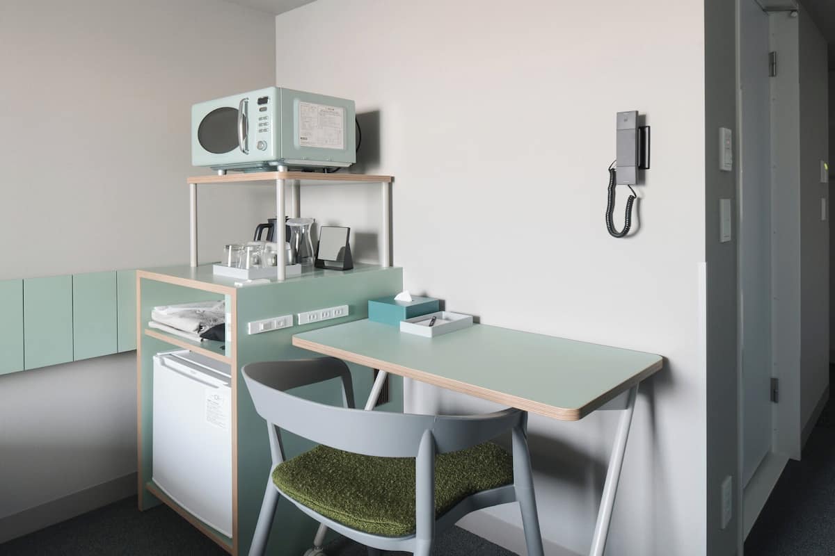 Una kitchenette compacta con microondas, un refrigerador pequeño y una silla con cojín verde.