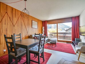 Ein Zimmer mit Holzwand, einem Esstisch mit Stühlen, einer Couch, einem Fernseher und Bergblick durch große Fenster.