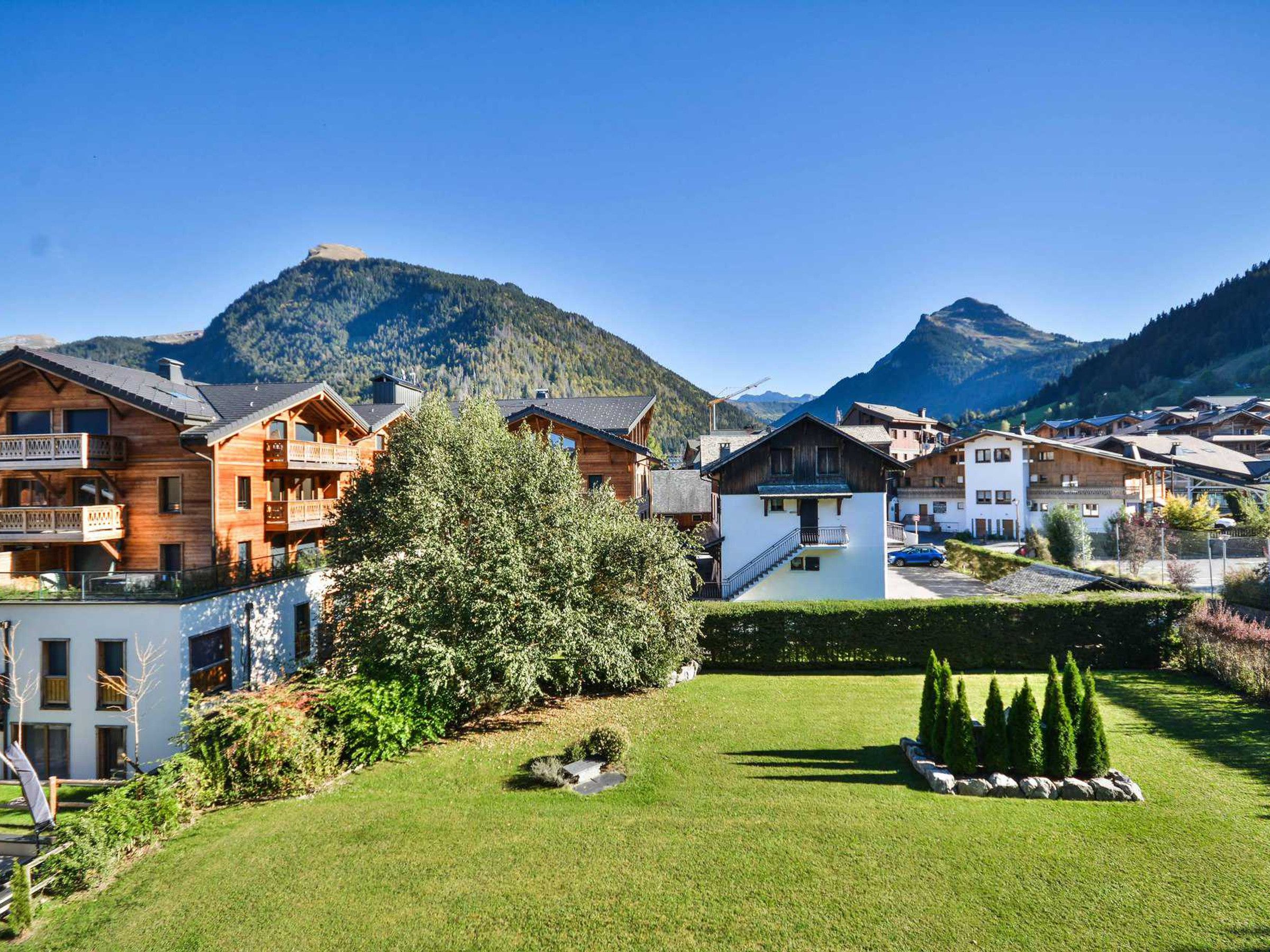 A mountain village with wooden houses, a grassy courtyard, and mountains in the background.