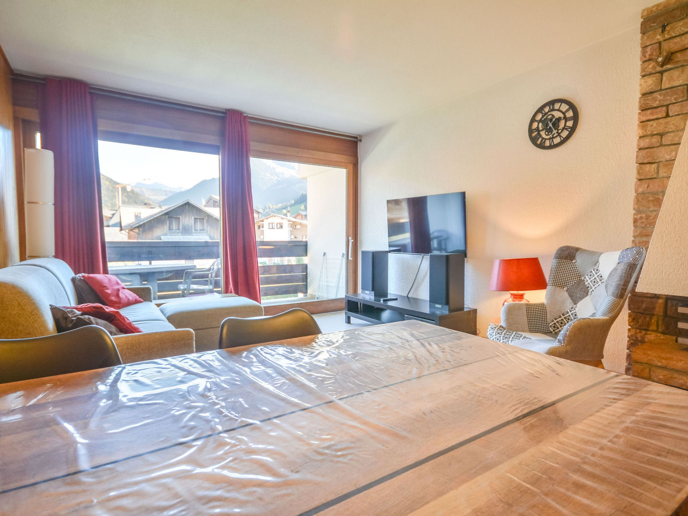 A hotel room with a bed, a television, a table, and a view of the mountains through the window.