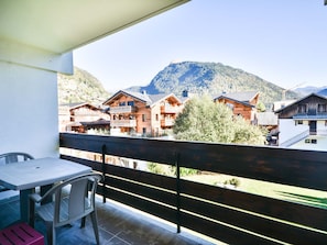 A balcony with a table and chairs, overlooking a mountain and traditional wooden buildings.