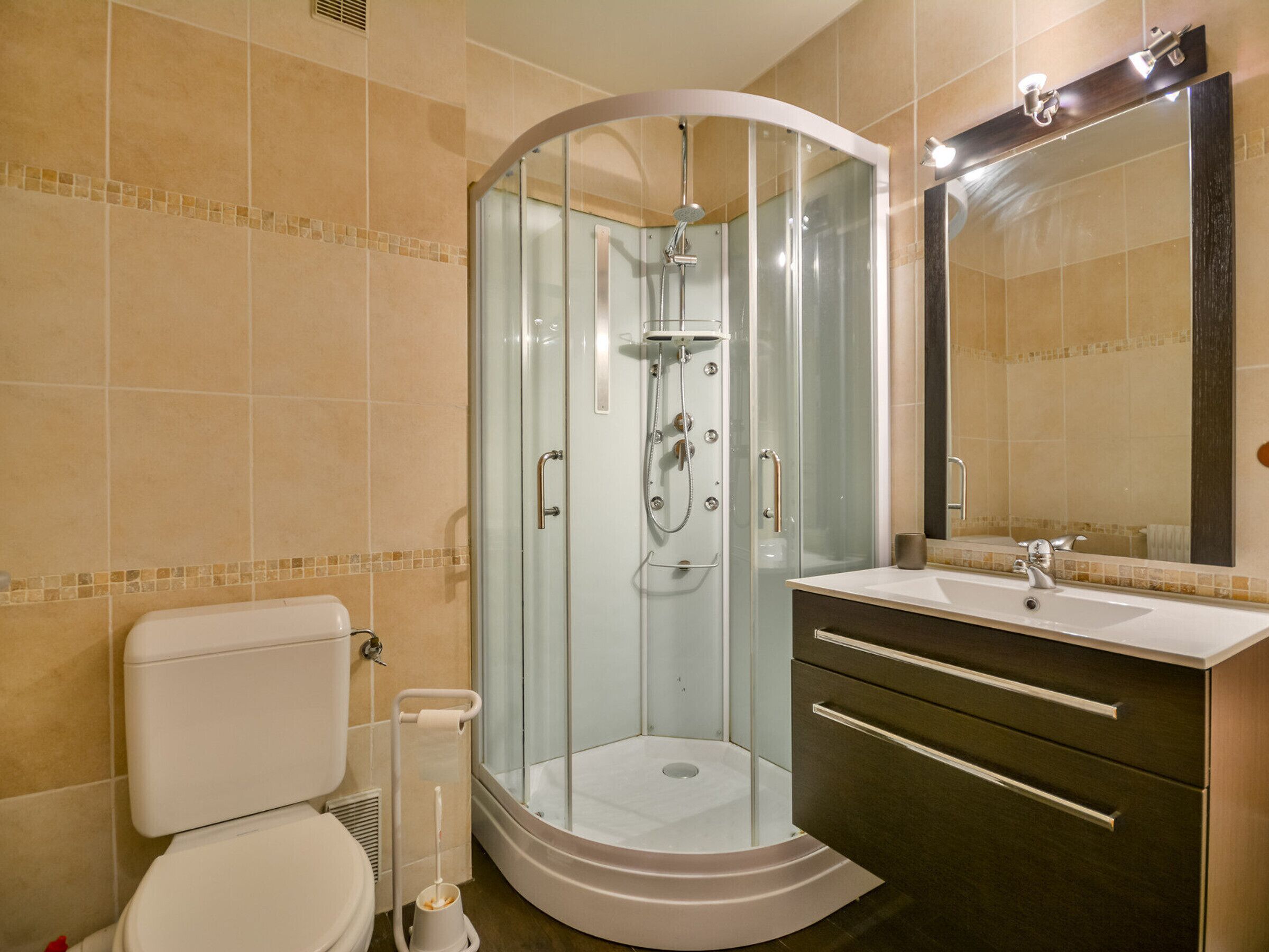 A modern bathroom with a glass-enclosed shower, a toilet, a sink with a mirror, and a vanity with drawers.