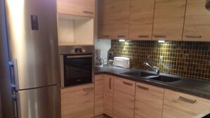 Eine Küche mit Holzschränken, einem Edelstahl-Kühlschrank, einem eingebauten Backofen, einer Spüle und einer gefliesten Rückwand.