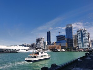 Un paisaje urbano frente al agua, con modernos rascacielos, un puerto deportivo y un cielo azul despejado.