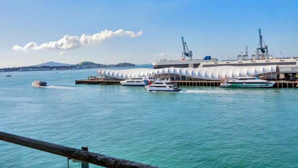 Un terminal situé au bord de l’eau, avec un grand bâtiment blanc, de nombreux bateaux amarrés et un ciel bleu dégagé.