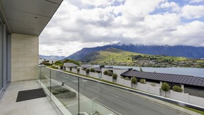 Un edificio moderno con un balcón de cristal que ofrece vistas a un lago, montañas y un pueblo.