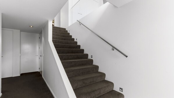 A staircase with carpeted steps and a metal handrail, leading to an upper floor.