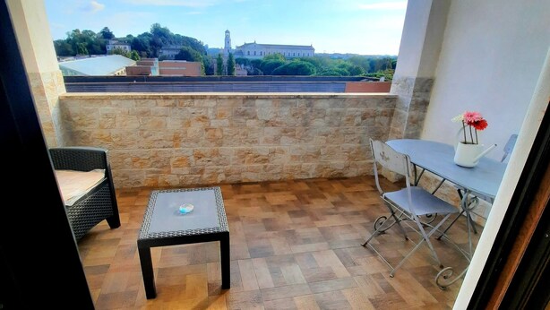 A balcony with a stone wall, a table with chairs, and a view of a building and trees. - Penthouse with stunning views of St. Paul's Basilica (Roma)