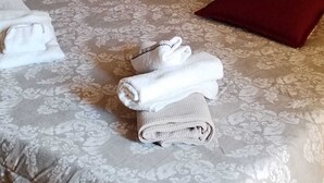 A neatly made bed with floral-patterned bedding, two red pillows, and rolled towels. - Penthouse with stunning views of St. Paul's Basilica (Roma)