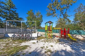 Explore the playground area with a climbing tower and slide, surrounded by trees and bike parking.
