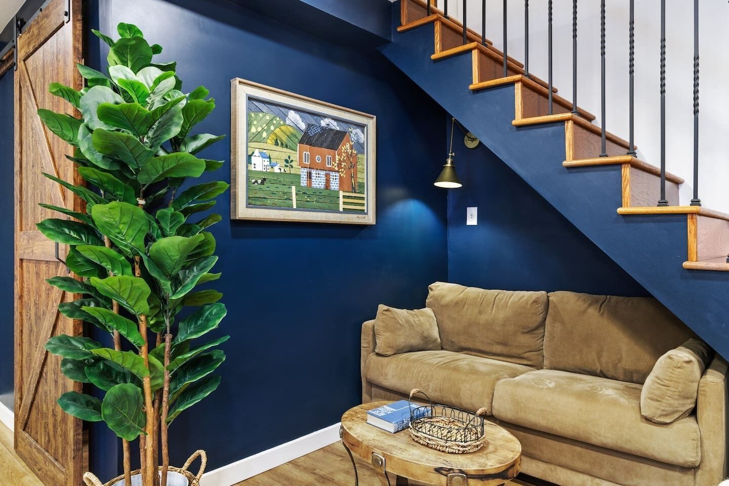 A living room with a blue wall, a beige sofa, a wooden staircase, and a framed painting.