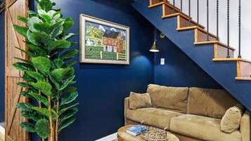 A living room with a blue wall, a beige sofa, a wooden staircase, and a framed painting.