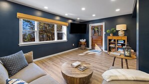 Ein modernes Wohnzimmer mit dunkelblauer Wand, Holzboden, einer Couch, einem Couchtisch und einem Bücherregal.