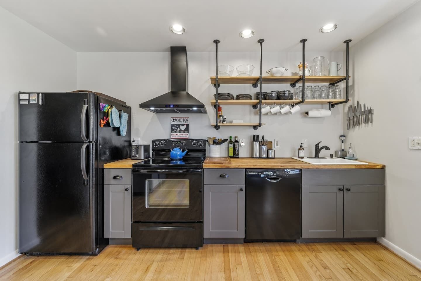 A modern kitchen with a black refrigerator, stainless steel appliances, wooden countertops, and built-in shelves for dishes.