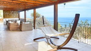 A wooden deck with a hammock, wicker furniture, and a view of the ocean.
