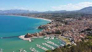 A coastal cityscape with a marina filled with boats, surrounded by residential buildings and mountains in the background.