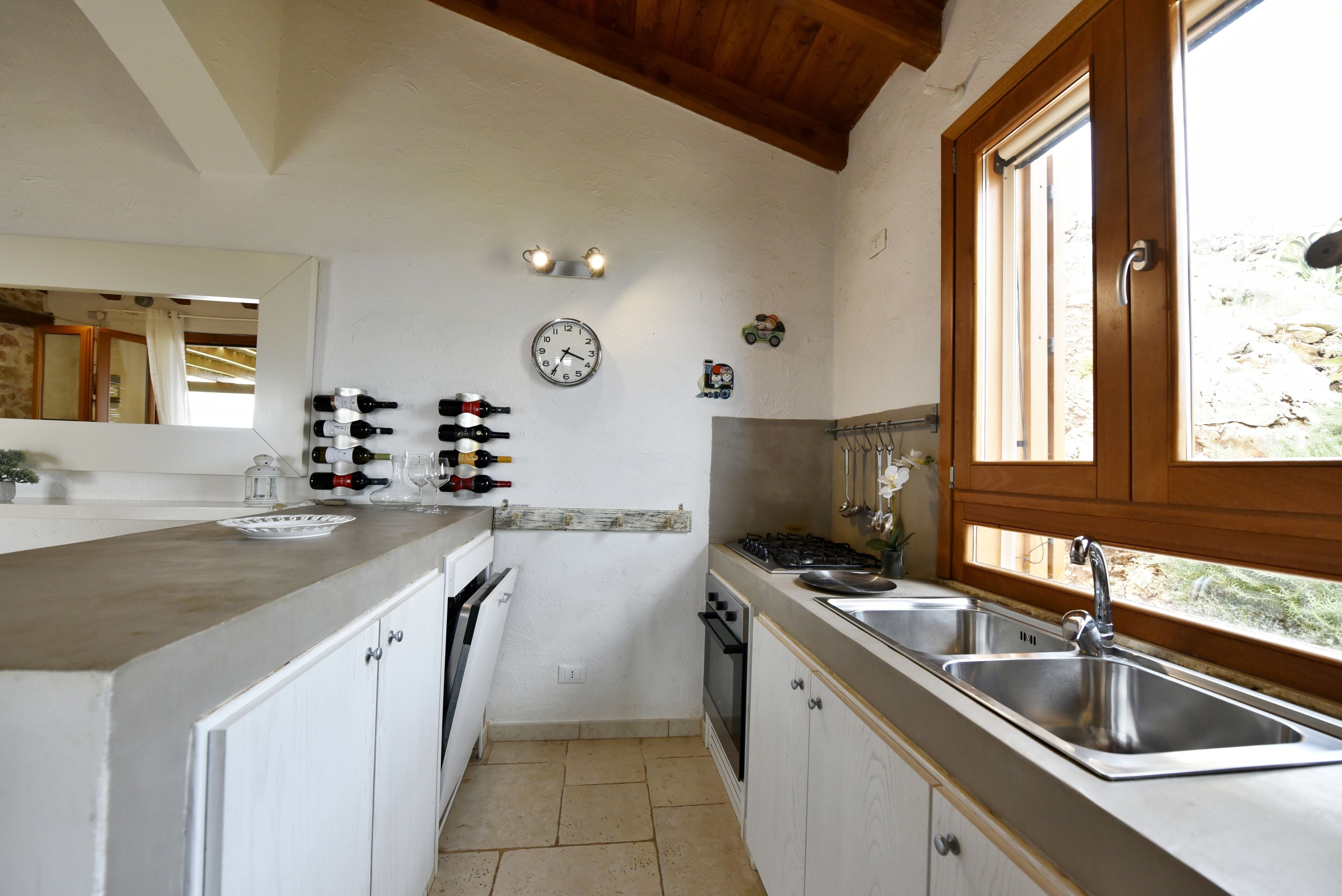 Una cocina con armarios blancos, estufa, fregadero y ventana con vistas al exterior.