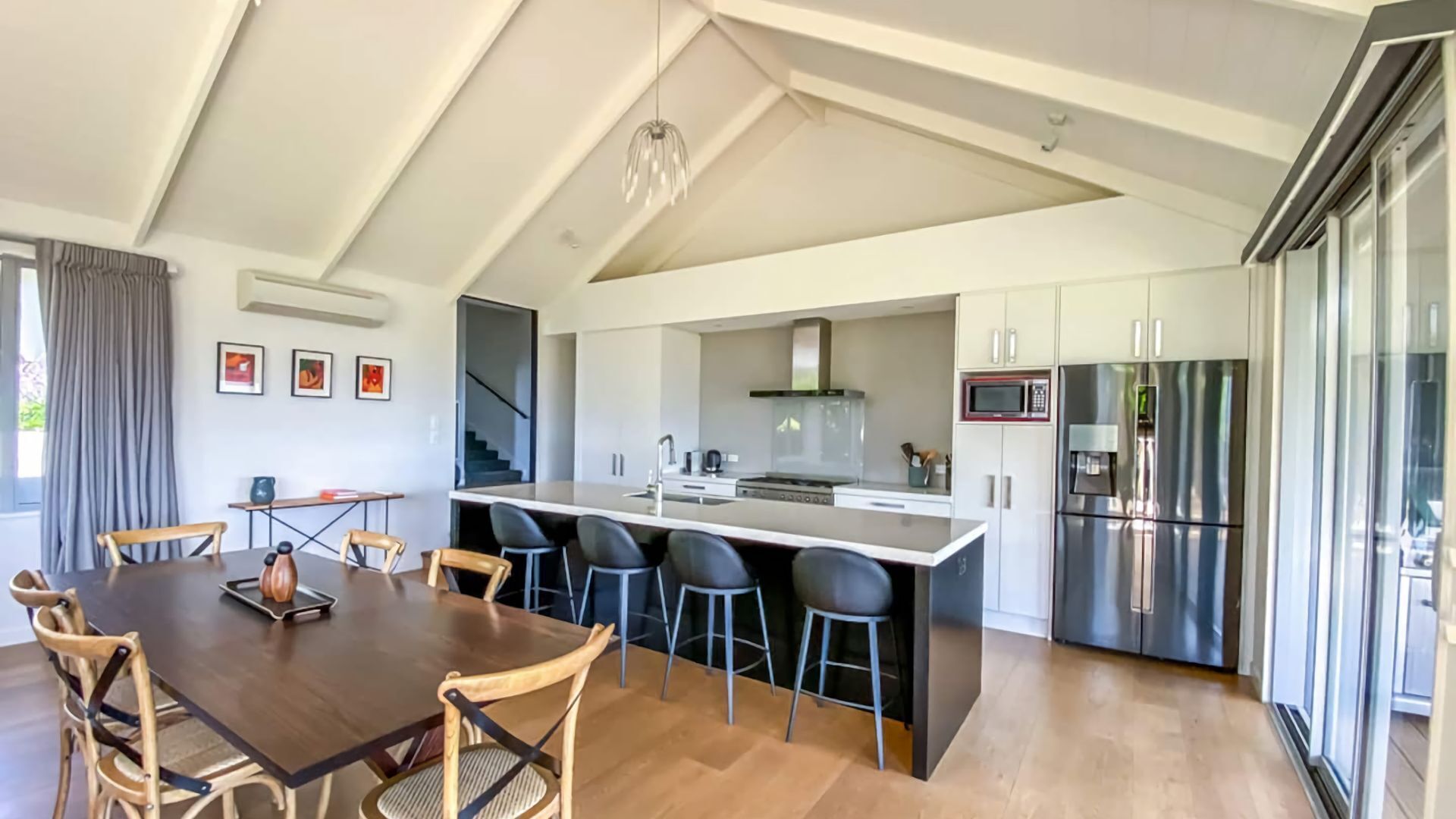 A modern kitchen with a central island, stainless steel appliances, and a dining area with wooden chairs.