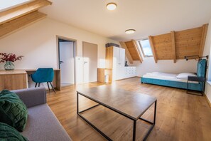 Een moderne loft slaapkamer met een schuine plafond, een houten bureau, een blauwe stoel, een bed met een blauw hoofdbord, en een klein raam.
