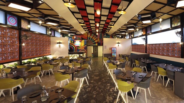 Un restaurant au décor moderne, avec un espace central aménagé en tables et chaises, entouré de murs ornés de panneaux décoratifs et d’une fresque colorée.