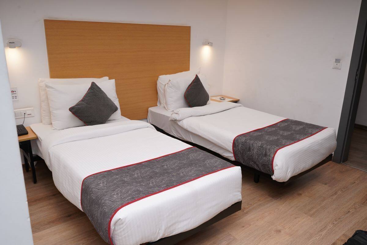 Habitación de hotel con dos camas individuales, cabecero de madera, mesitas de noche y una mesita auxiliar.